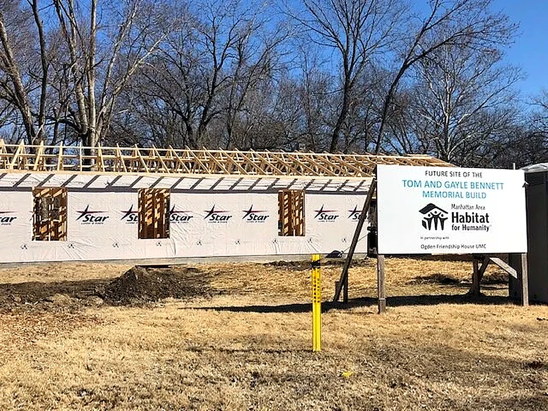 Framed house with roof trusses beside a Manhattan Area Habitat for Humanity sign